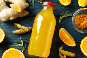 Orange juice in a glass bottle surrounded by nutrient dense food to target immune health